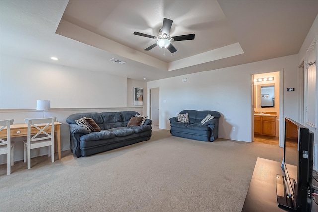 living area featuring a raised ceiling, a ceiling fan, visible vents, and light carpet