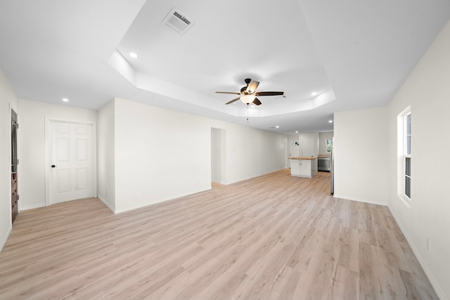 unfurnished living room with visible vents, ceiling fan, baseboards, a tray ceiling, and light wood-style flooring