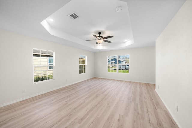 unfurnished room featuring a ceiling fan, visible vents, light wood finished floors, baseboards, and a raised ceiling