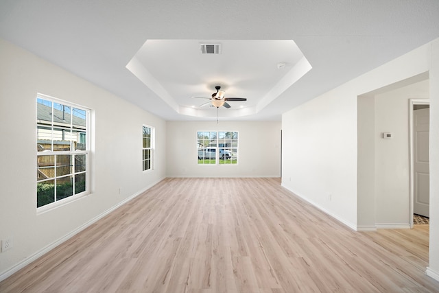 spare room with light wood finished floors, visible vents, baseboards, a raised ceiling, and a ceiling fan