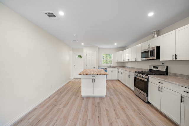 kitchen featuring visible vents, a kitchen island, stainless steel appliances, wood counters, and a sink