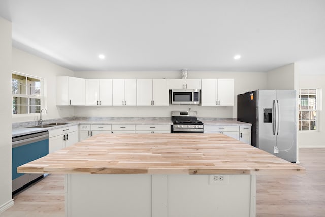 kitchen with butcher block countertops, white cabinetry, stainless steel appliances, and a sink