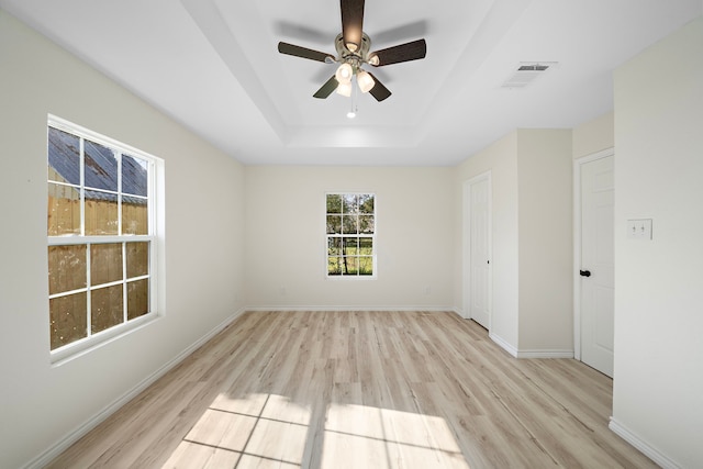 unfurnished room featuring visible vents, baseboards, a tray ceiling, light wood-style flooring, and a ceiling fan