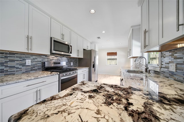 kitchen featuring light stone counters, a sink, decorative backsplash, appliances with stainless steel finishes, and white cabinetry