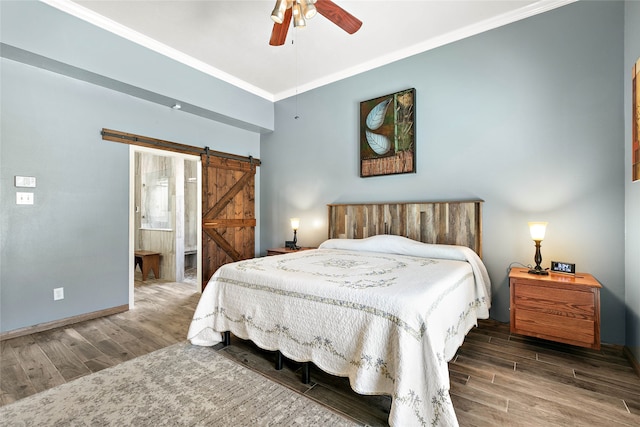 bedroom featuring wood finished floors, baseboards, ensuite bath, crown molding, and a barn door