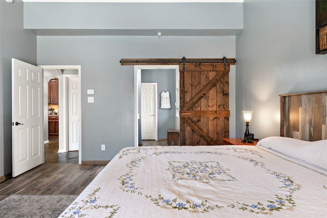 bedroom featuring a barn door, dark wood-style floors, and baseboards