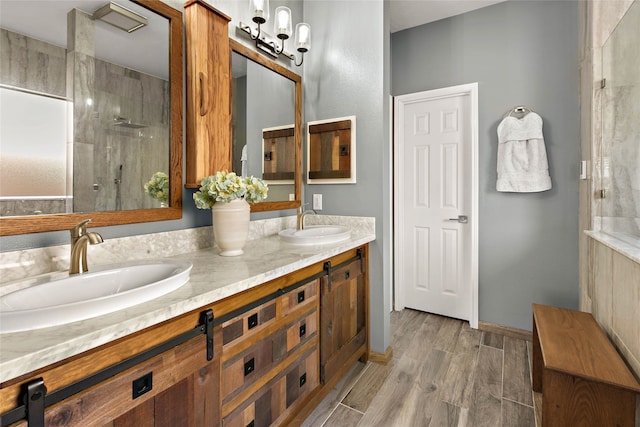 full bathroom with wood finished floors, tiled shower, double vanity, and a sink