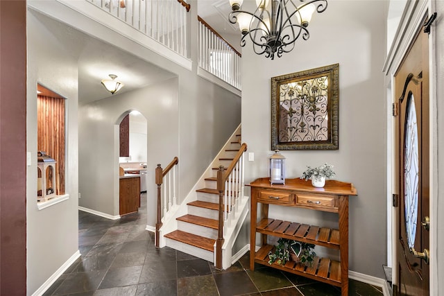 foyer entrance with baseboards, an inviting chandelier, a high ceiling, arched walkways, and stairs