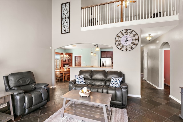 living area with baseboards, arched walkways, a towering ceiling, and a chandelier