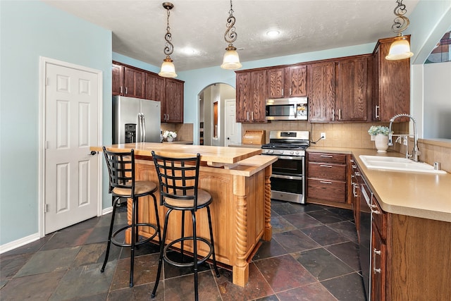 kitchen featuring butcher block countertops, a sink, stone tile floors, arched walkways, and appliances with stainless steel finishes