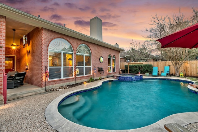 pool at dusk featuring a ceiling fan, a patio area, fence, and a pool with connected hot tub