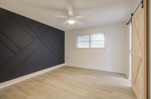 spare room featuring baseboards, a ceiling fan, light wood-type flooring, and a barn door