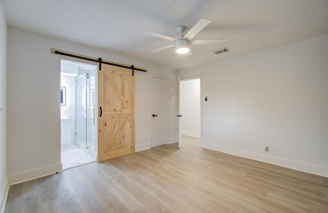 unfurnished bedroom featuring baseboards, visible vents, light wood-style floors, a textured ceiling, and a barn door