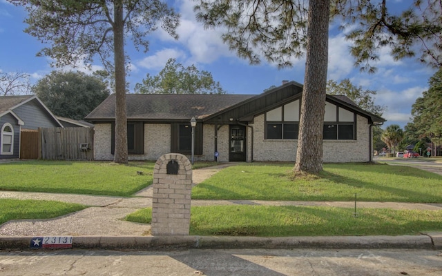 mid-century home with brick siding, roof with shingles, a front yard, and fence