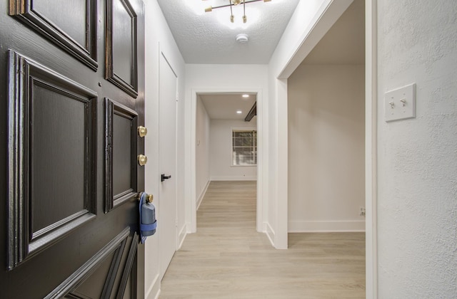 entryway featuring baseboards, light wood finished floors, and a textured ceiling