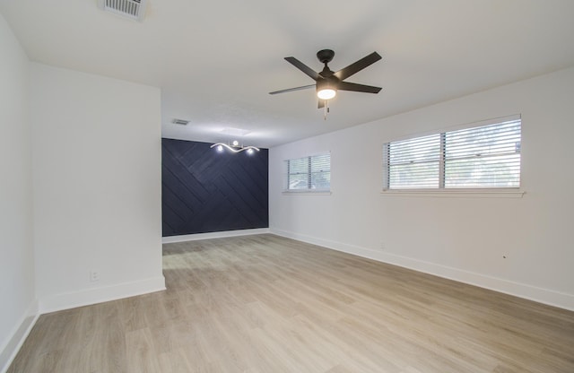 spare room with visible vents, an accent wall, baseboards, light wood-type flooring, and a ceiling fan