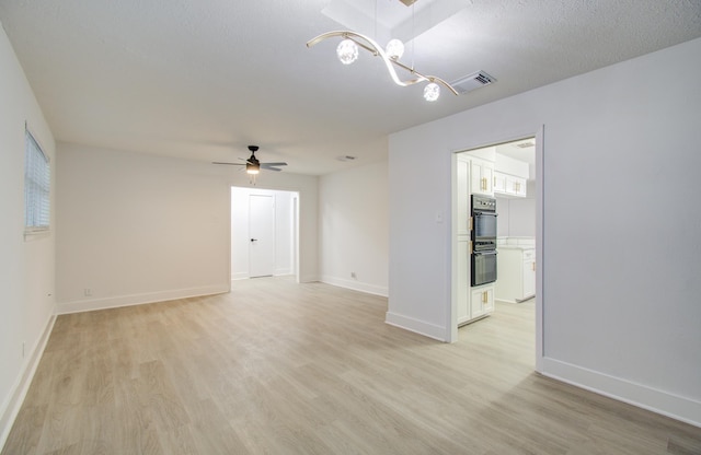 empty room featuring visible vents, ceiling fan with notable chandelier, baseboards, and light wood finished floors