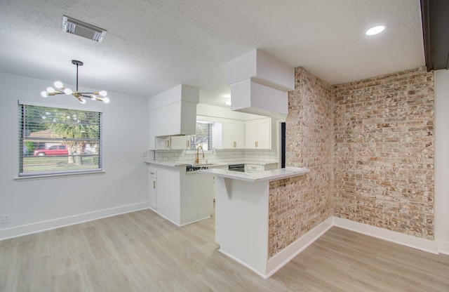 kitchen featuring light wood finished floors, visible vents, light countertops, a peninsula, and a notable chandelier