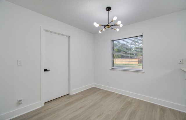 spare room with baseboards, light wood-style floors, a chandelier, and a textured ceiling