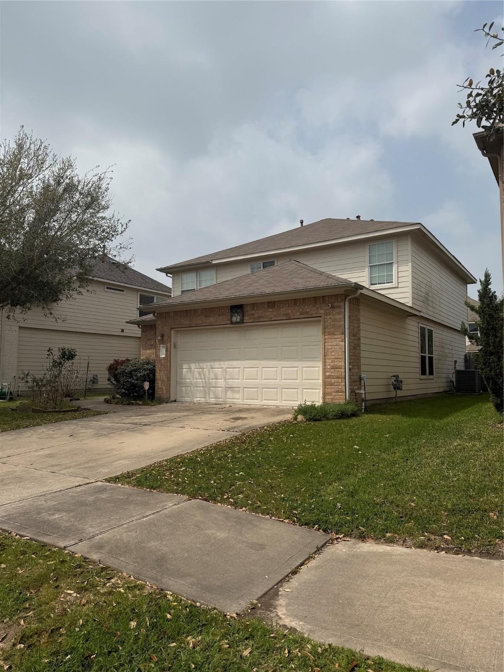 view of side of home with a yard, brick siding, central AC unit, and concrete driveway