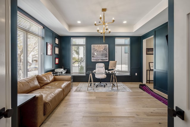 office area with a wealth of natural light, light wood-style flooring, a raised ceiling, and a chandelier