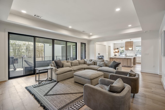 living area featuring visible vents, light wood-type flooring, and a tray ceiling