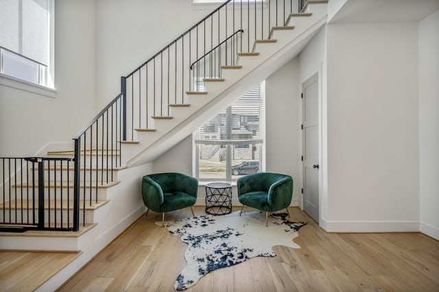 living area featuring a towering ceiling, baseboards, wood finished floors, and stairs