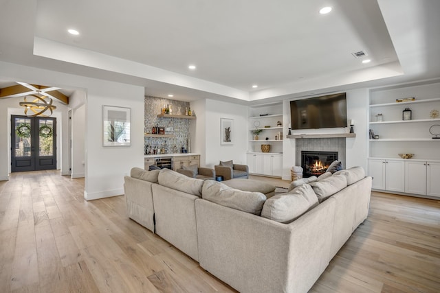 living area featuring a tray ceiling, a glass covered fireplace, recessed lighting, light wood-style floors, and a bar