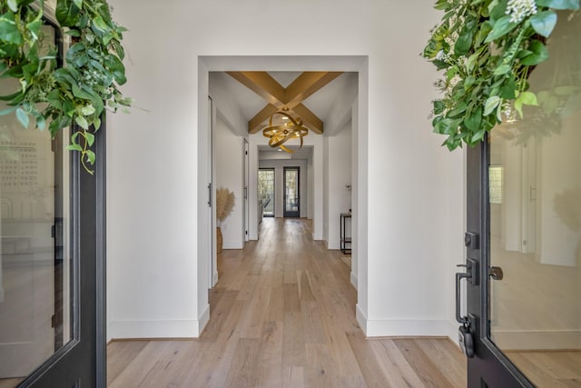 hallway with a notable chandelier, baseboards, and light wood-style floors