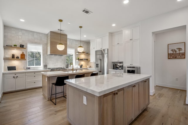 kitchen with visible vents, a center island with sink, appliances with stainless steel finishes, custom exhaust hood, and open shelves