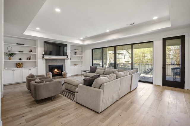 living room with visible vents, a warm lit fireplace, light wood-type flooring, and a raised ceiling