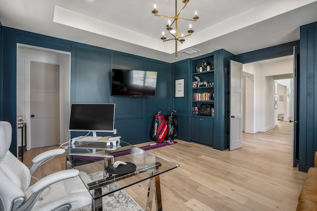 office featuring a tray ceiling, a decorative wall, light wood finished floors, and a chandelier