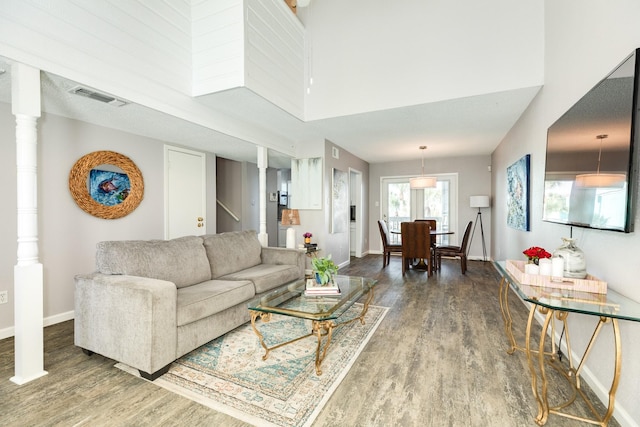 living room featuring wood finished floors, visible vents, a towering ceiling, and baseboards