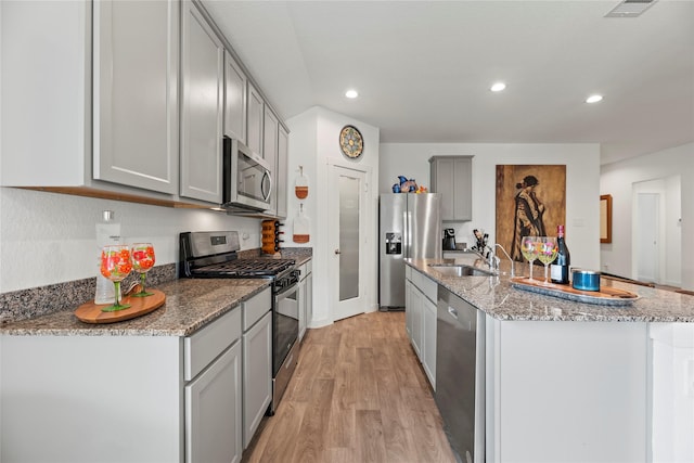 kitchen with a sink, gray cabinetry, light wood-style flooring, appliances with stainless steel finishes, and a kitchen island with sink