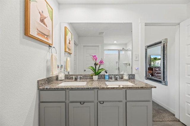 full bathroom featuring double vanity, a stall shower, baseboards, and a sink