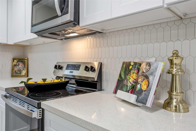 kitchen with decorative backsplash, white cabinets, light stone countertops, and stainless steel appliances