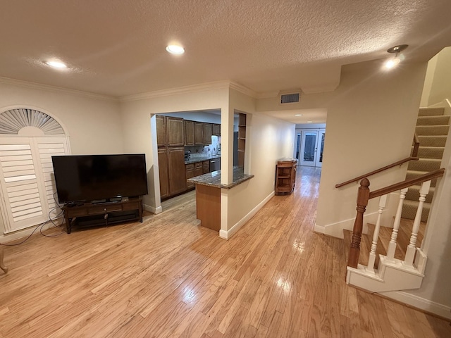 living area featuring visible vents, light wood-style flooring, a textured ceiling, baseboards, and stairs