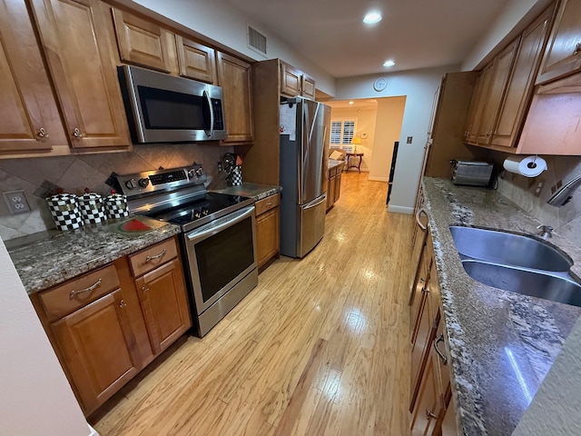 kitchen with light wood finished floors, visible vents, decorative backsplash, appliances with stainless steel finishes, and a sink