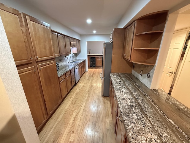 kitchen featuring light wood-type flooring, decorative backsplash, dark stone countertops, stainless steel appliances, and a sink