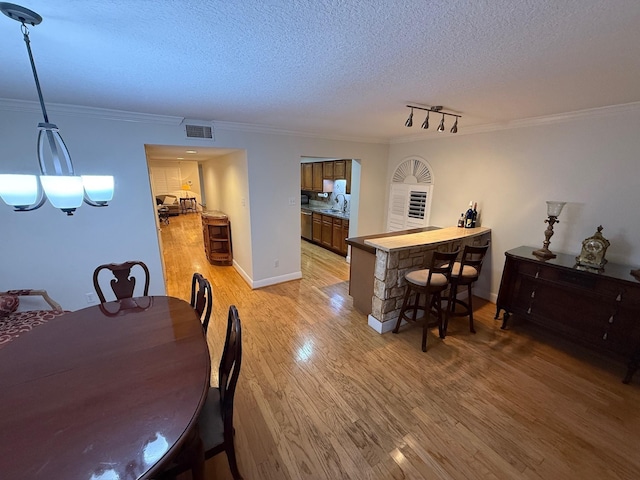 dining room with baseboards, visible vents, light wood-style flooring, ornamental molding, and a textured ceiling