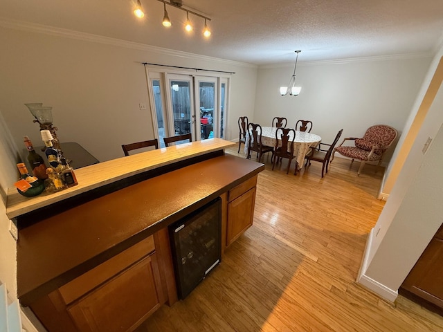 bar with crown molding, decorative light fixtures, beverage cooler, and light wood finished floors