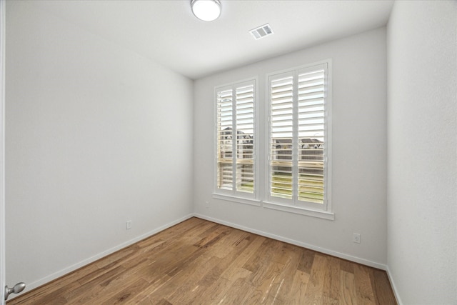 empty room featuring wood finished floors, visible vents, and baseboards