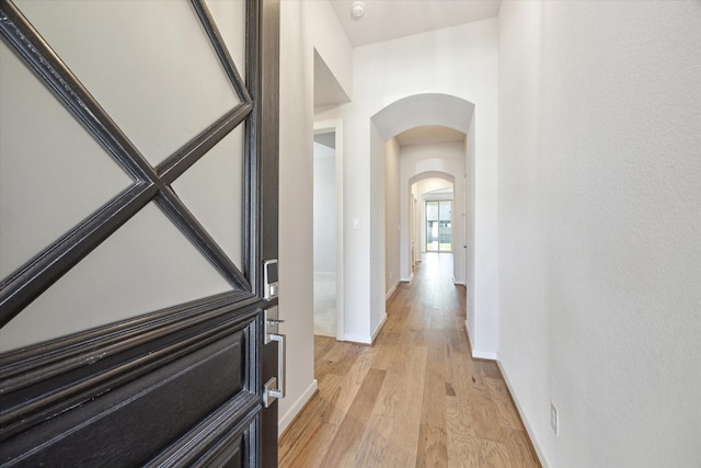 hall featuring baseboards, arched walkways, and light wood finished floors