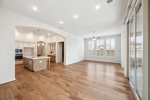 kitchen with visible vents, a kitchen island with sink, a sink, open floor plan, and appliances with stainless steel finishes