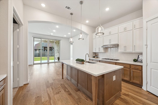 kitchen with visible vents, light wood-type flooring, under cabinet range hood, a sink, and stainless steel gas stovetop