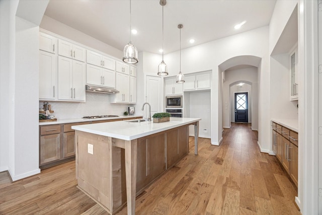 kitchen with built in microwave, under cabinet range hood, light wood-style flooring, arched walkways, and gas stovetop