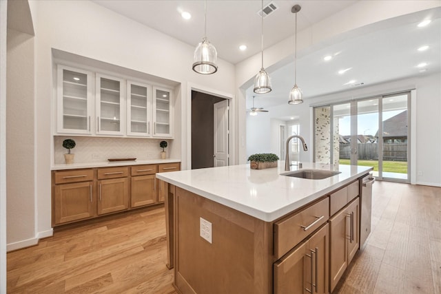 kitchen featuring light wood-style flooring, a sink, decorative light fixtures, brown cabinets, and backsplash