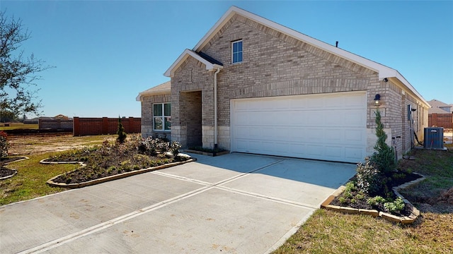 view of front of house with driveway, fence, an attached garage, brick siding, and central AC unit