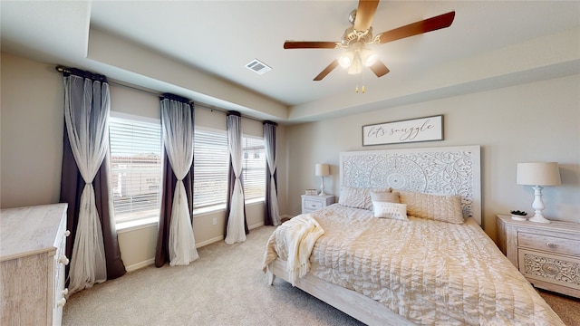 bedroom with a ceiling fan, visible vents, baseboards, a raised ceiling, and light colored carpet