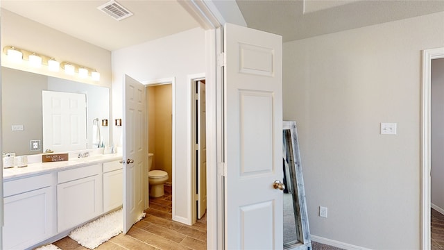 bathroom featuring wood finish floors, visible vents, a sink, double vanity, and baseboards